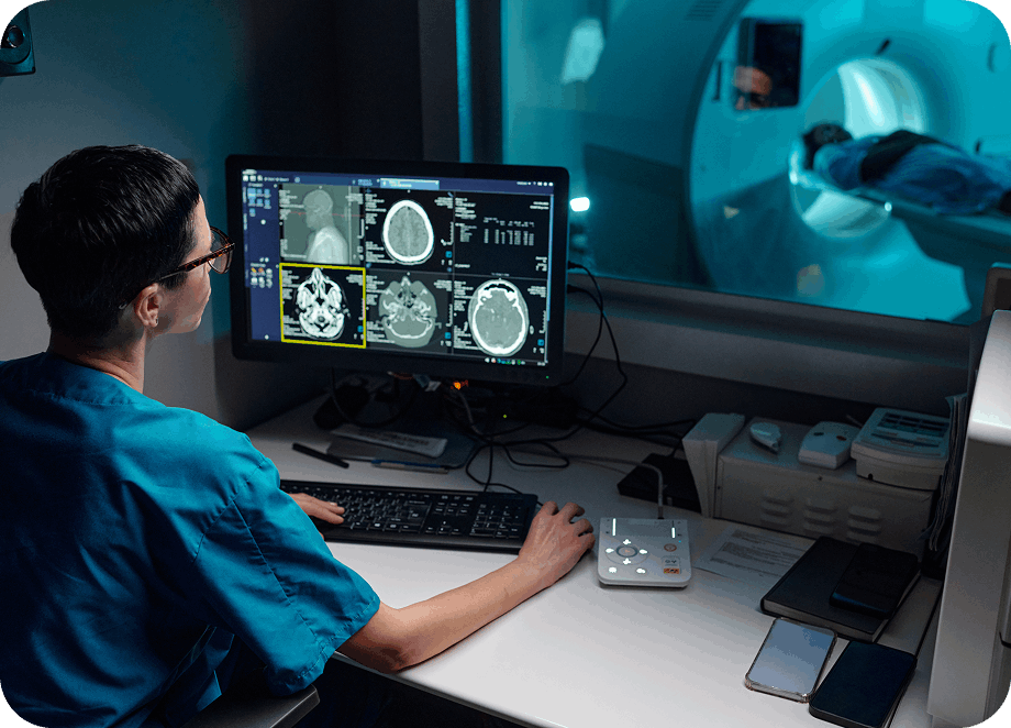 man looking at scans on computer with MRI happening in background